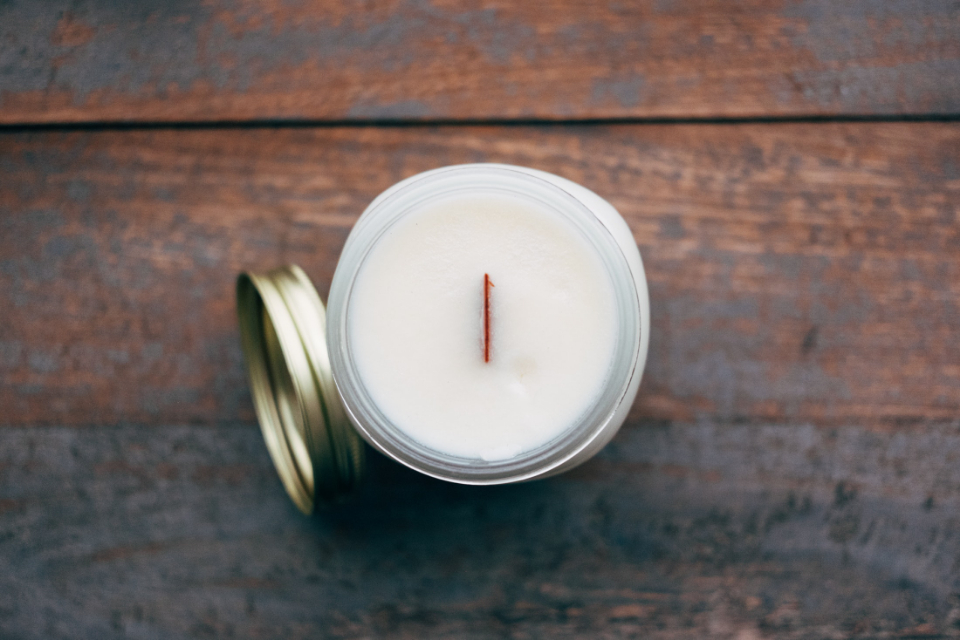 A white candle in a glass jar on a wooden surface — the capsule vanity philosophy of owning fewer, better beauty essentials