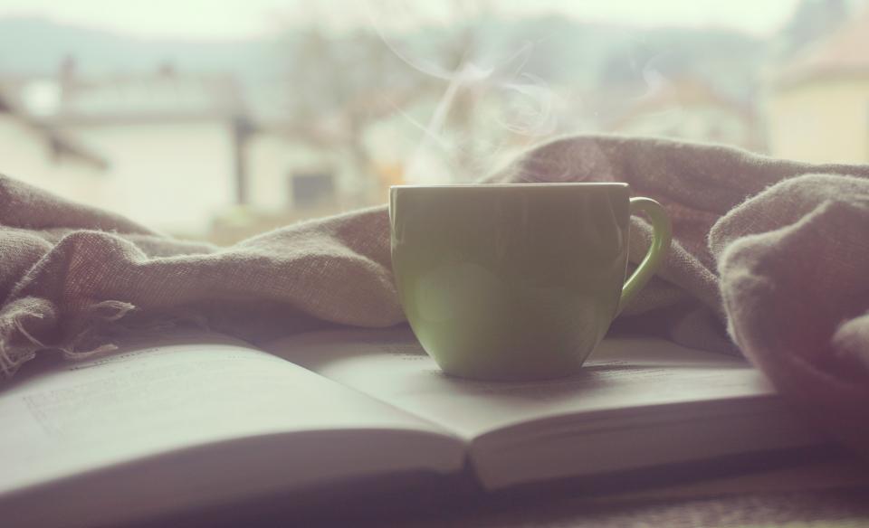 A steaming cup of coffee resting on an open book — the reading ritual behind the best books for reinventing yourself