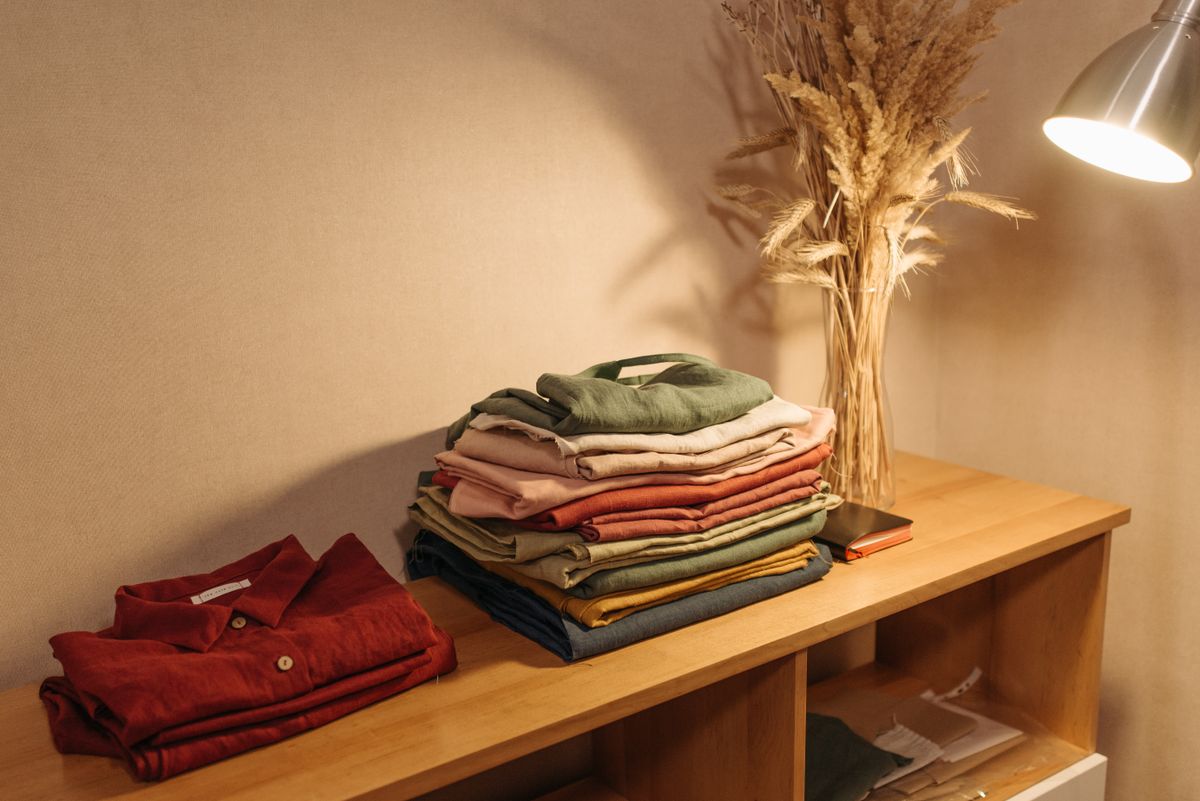 Stack of folded organic-fiber textiles in warm earth tones on a wooden shelf