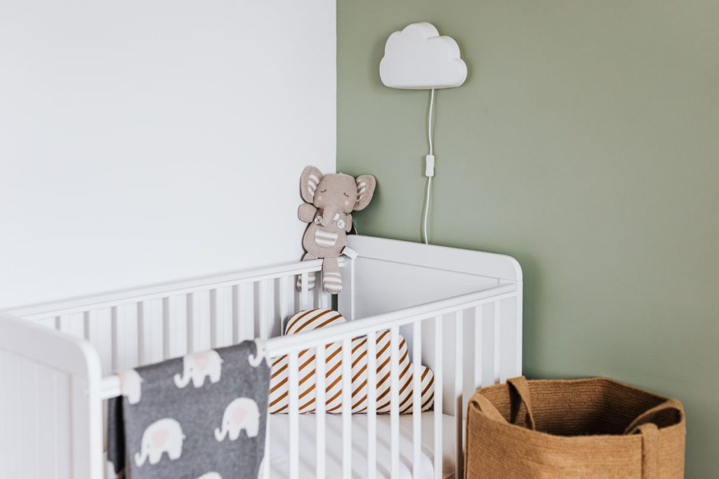 Non-toxic nursery with a white crib, sage-green wall, and organic-toned decor in soft natural light