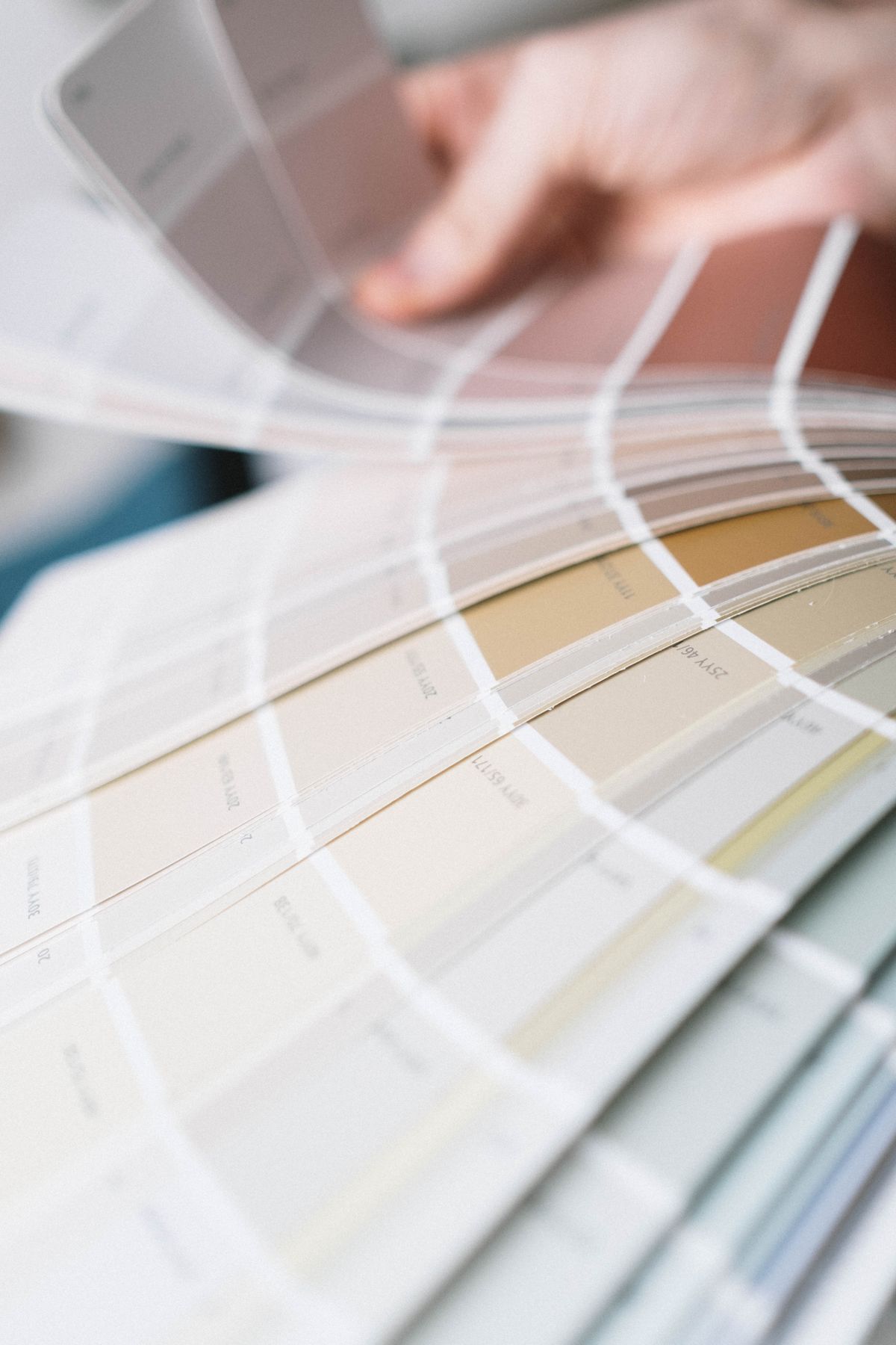 Hand fanning through a paint color swatch deck in soft neutral tones